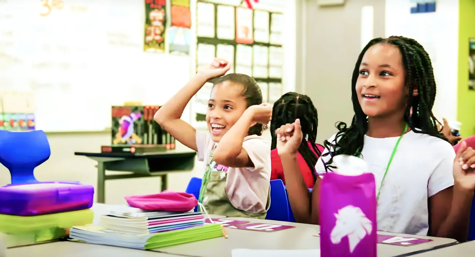 Two girls raise their fists and cheer at their classroom desks